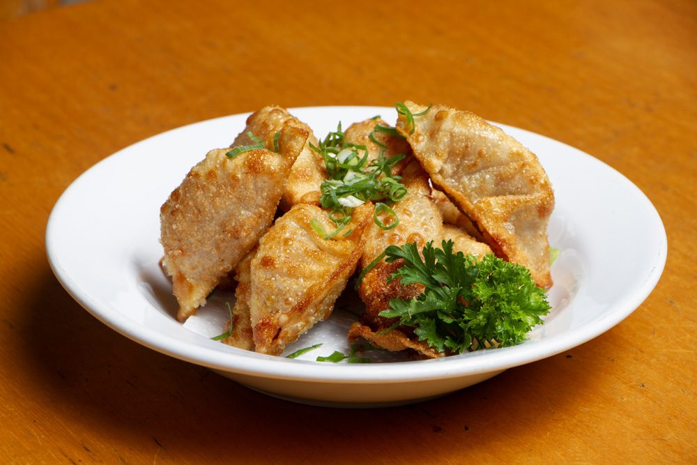 Porção de guiozas, pastéis chineses fritos e dourados, servidos em prato sobre mesa de madeira